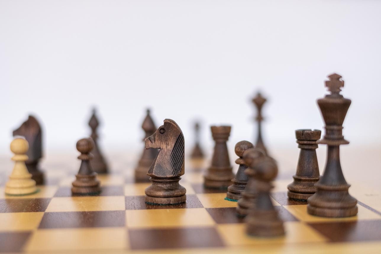 Nahaufnahme von Schachfiguren auf einem Schachbrett mit verschiedenen Holzfarben. Im Fokus steht ein Springer.